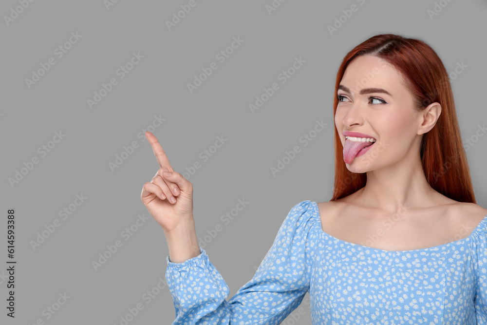 Happy woman showing her tongue and pointing at something on gray background. Space for text Happy woman showing her tongue and pointing at something on gray background. Space for text