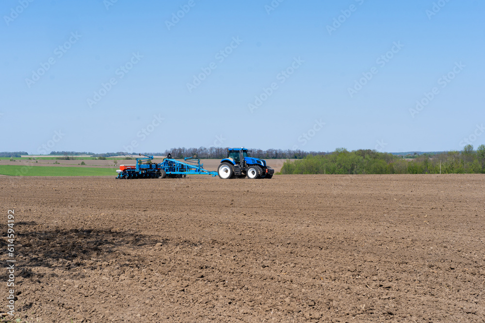 Obraz premium The tractor drives across the field and cultivates the land. Agricultural vehicle works in countryside. Sowing is the process of planting seeds in the ground as part of the early spring time