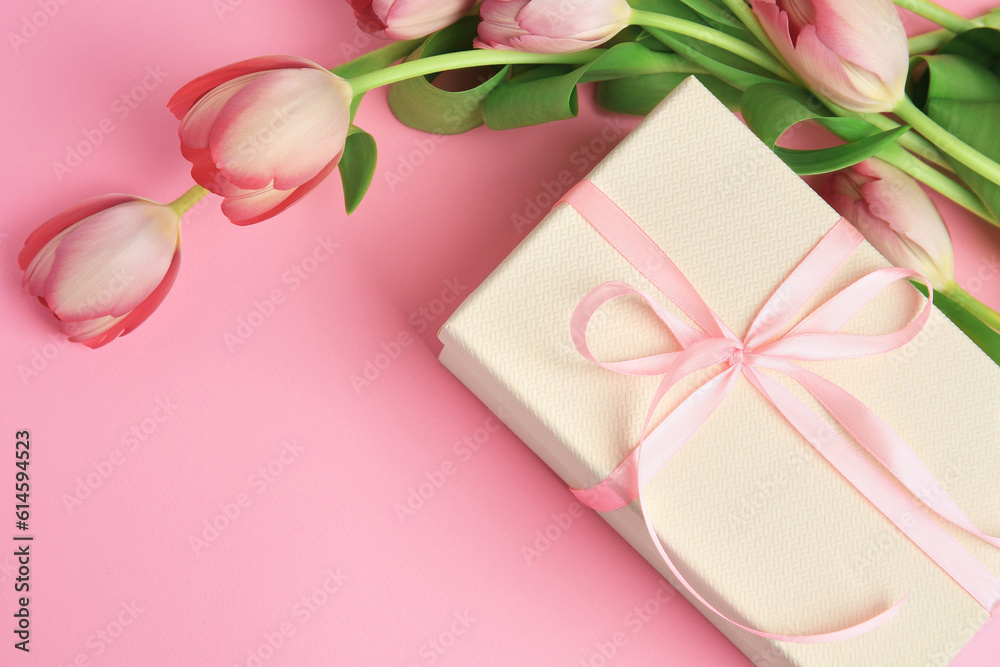 Beautiful gift box with bow and tulips on pink background, above view. Space for text