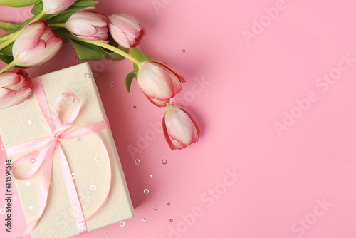 Beautiful gift box with bow, tulips and confetti on pink background, flat lay. Space for text © New Africa