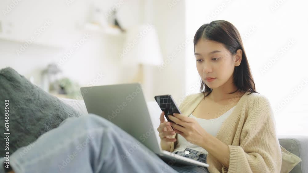 Young asian woman using computer laptop and mobile smartphone while seated on couch at home Young asian woman using computer laptop and mobile smartphone while seated on couch at home