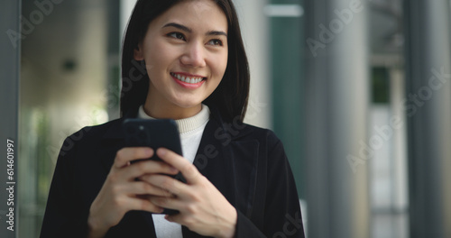 Young Asian businesswoman in suit holding smartphone and a folder while walking