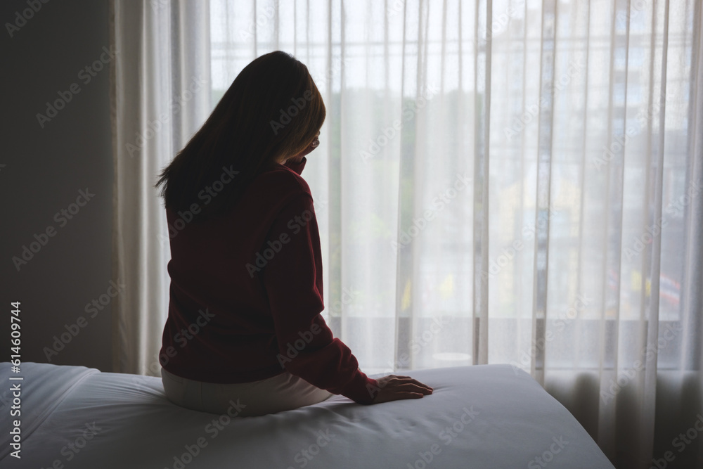 Silhouette of a woman sitting and crying on a bed in bedroom Silhouette of a woman sitting and crying on a bed in bedroom