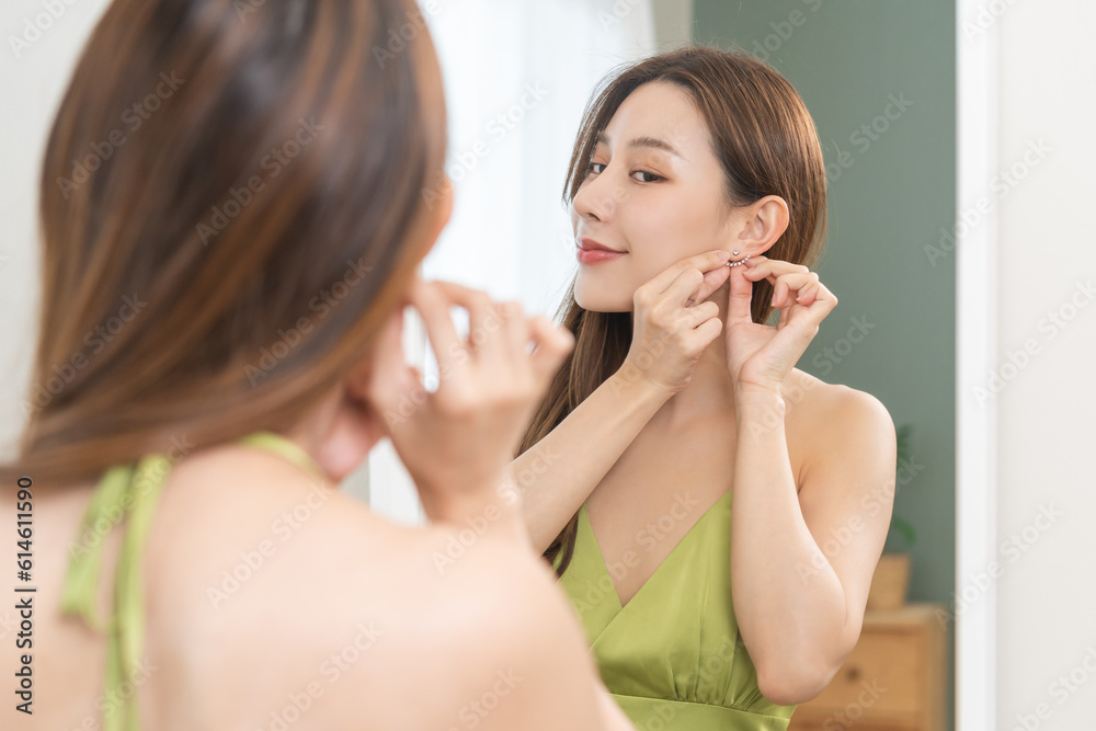 Get dress, elegant asian young woman with makeup glamour, getting ready wearing green cloth, gorgeous female putting earring or jewelry looking into the mirror at home, prepare going event night party Get dress, elegant asian young woman with makeup glamour, getting ready wearing green cloth, gorgeous female putting earring or jewelry looking into the mirror at home, prepare going event night party