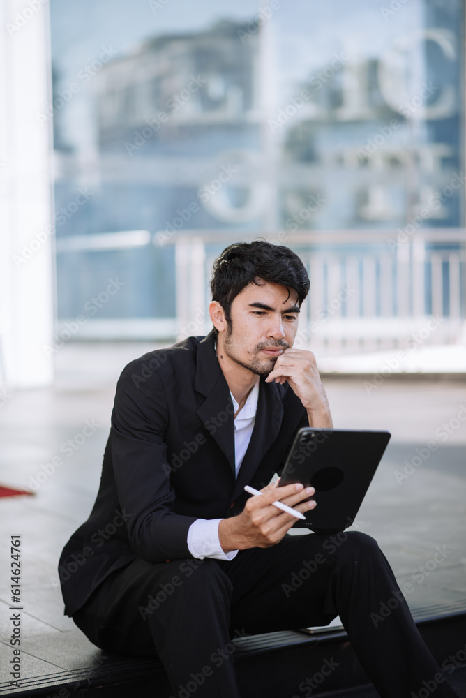 Asian businessman using a tablet on a bench in the city Asian businessman using a tablet on a bench in the city