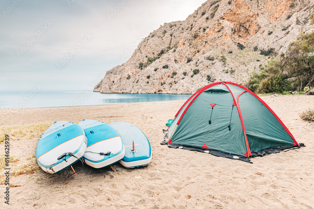 Camping tent with sup boards on the wild beach at mediterranean seacoast. Water trip and sportive recreation Camping tent with sup boards on the wild beach at mediterranean seacoast. Water trip and sportive recreation