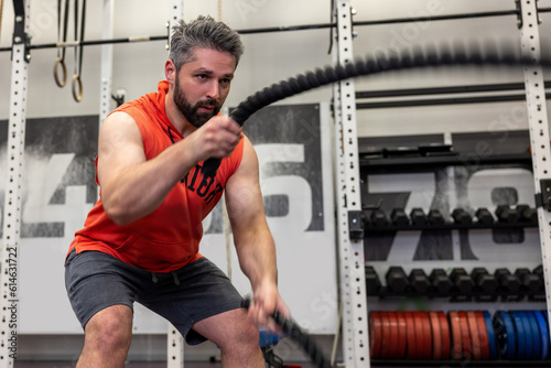 Strong powerful man working out with battle ropes at gym, developing strenth and endurance. photo