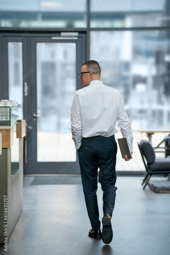 Back view of business man holding closed laptop wearing white shirt walking to cafe. Back view of business man holding closed laptop wearing white shirt walking to cafe.