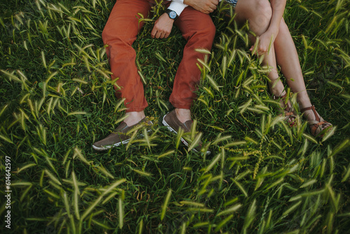 Couple sitting together on green grass. Boy's and girl's legs on green grass