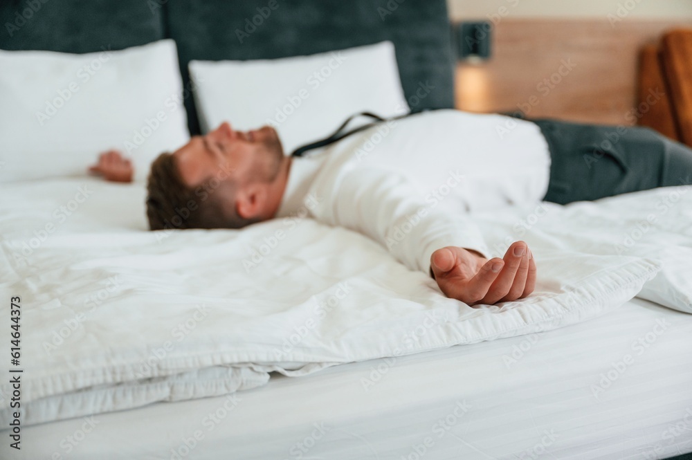 Tired, lying down on the bed. Businessman is indoors in the hotel room Tired, lying down on the bed. Businessman is indoors in the hotel room