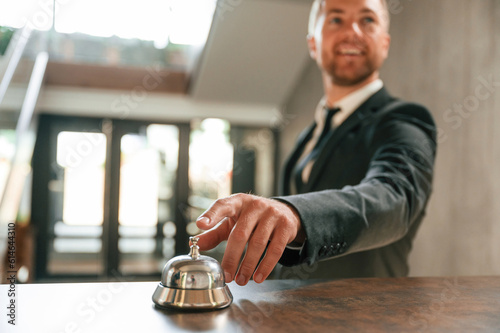 Standing, using hotel desk bell. A man in a black jacket at the hotel reception
