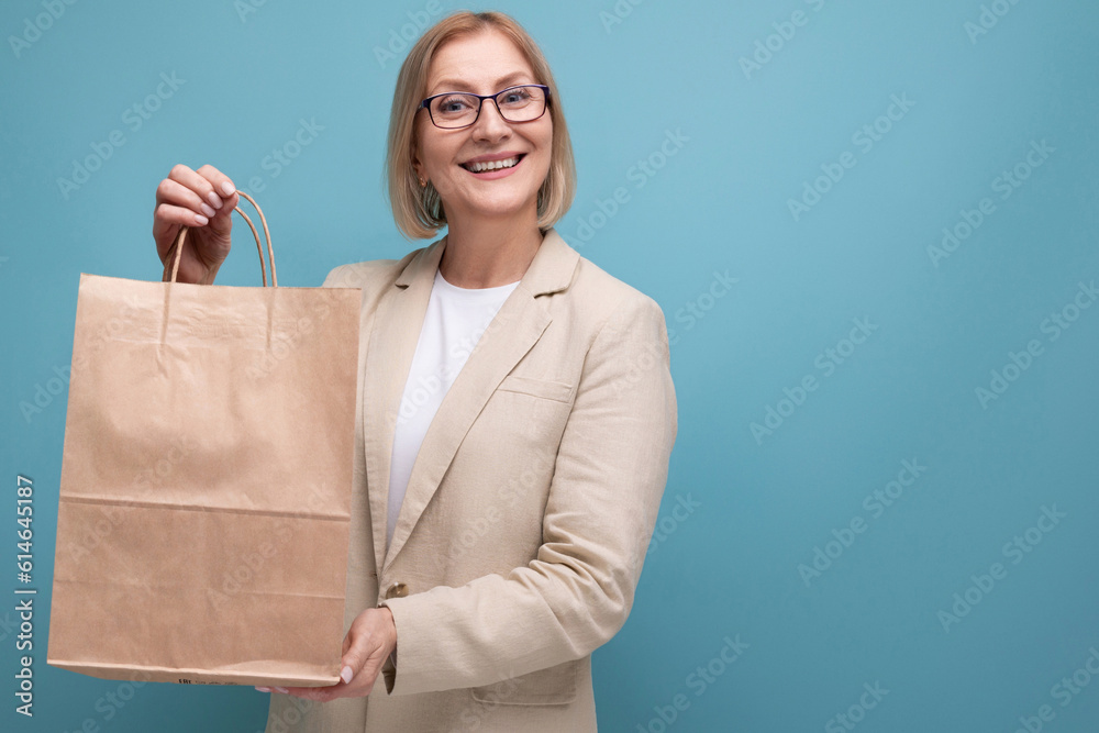 middle-aged business concept. smiling mature woman in jacket holding social package on studio background with copy space middle-aged business concept. smiling mature woman in jacket holding social package on studio background with copy space