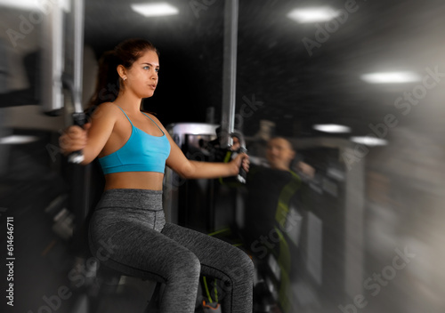 Sporty young woman using chest fly machine in gym