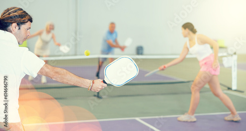 Rear view of sportive man with white racket playing pickleball tennis at court