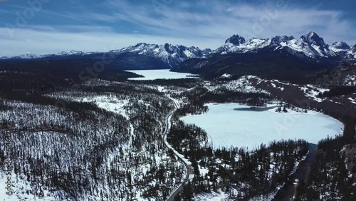 Frozen Redfish Lake Surrounded By Mountains And Forest In Winter Near Stanley In Idaho, USA. wide aerial photo