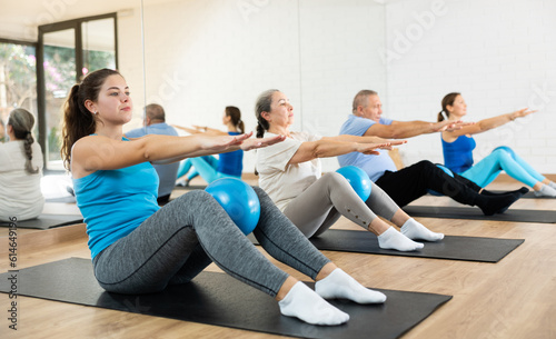 Sportive young woman doing pilates exercises with ball in gym area during workout session. Persons engaging in pilates in fitness room