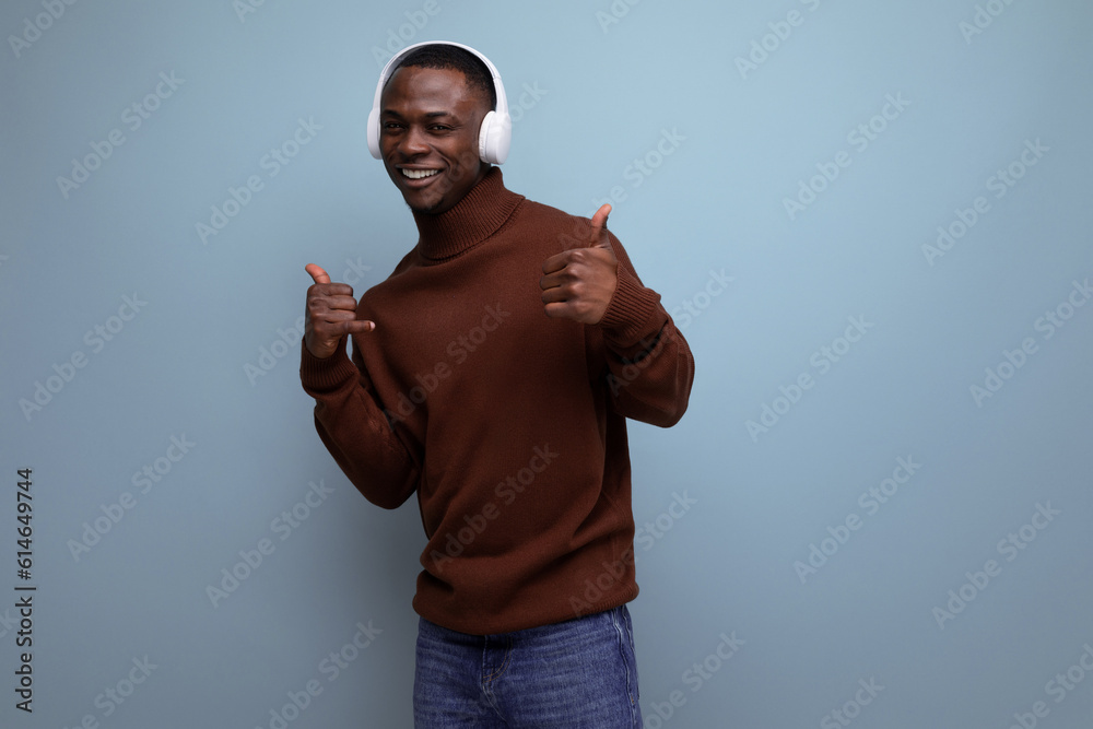 Naklejka premium handsome energetic young african man listening to music with headphones on the background with copy space