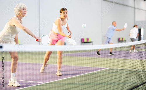 Two athletic women of different ages are playing a game of pickleball on a court inside a sports facility