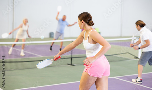 Rear view of young girl playing pickleball match on indoor court on blurred background of opponents. Sport and active lifestyle concept..