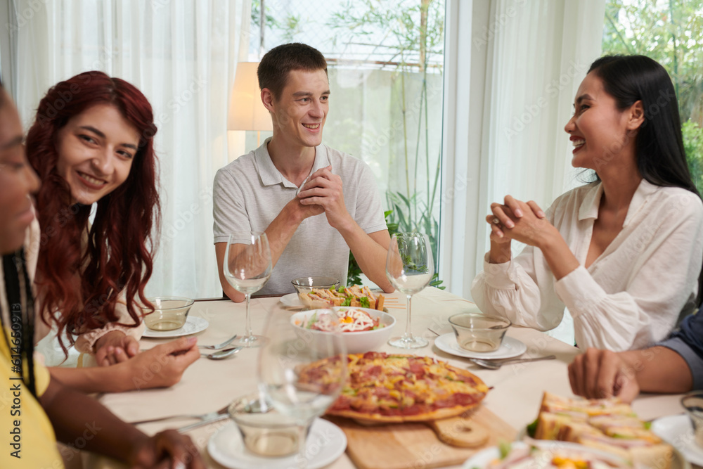 Group of happy friendly young people talking at dinner table