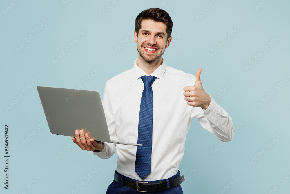 Young happy employee IT business man corporate lawyer wearing classic formal shirt tie work in office hold use aptop pc computer show thumb up isolated on plain light blue background studio portrait. Young happy employee IT business man corporate lawyer wearing classic formal shirt tie work in office hold use aptop pc computer show thumb up isolated on plain light blue background studio portrait.