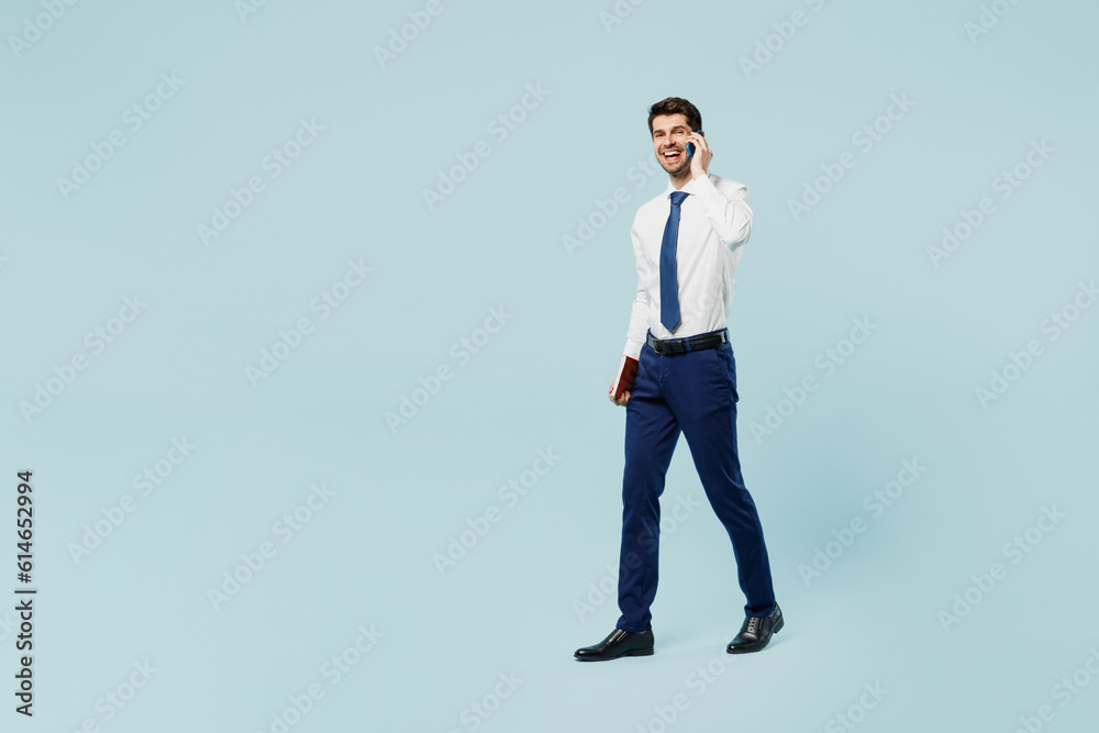 Full body young employee IT business man corporate lawyer wear classic formal shirt tie work in office talk speak on mobile cell phone isolated on plain pastel light blue background studio portrait. Full body young employee IT business man corporate lawyer wear classic formal shirt tie work in office talk speak on mobile cell phone isolated on plain pastel light blue background studio portrait.