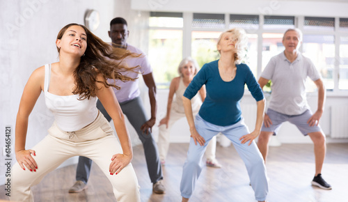 Girl dance teacher instruct group of elderly people to dance modern dances. Young woman moves freely and dance hip-hop with unfastened hair in fitness studio