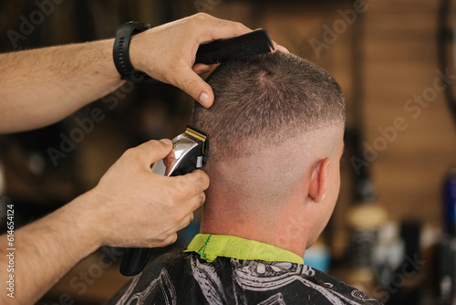 Back view of human hand hold trimmer and make hairstyle for man. Barbershop 
