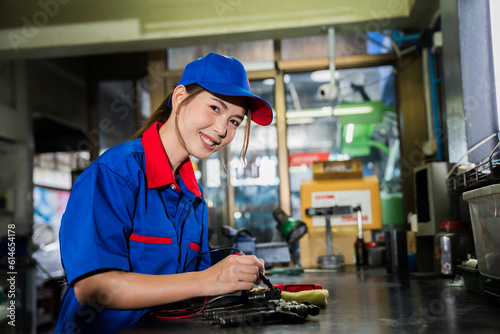 A female diesel engine mechanic in a blue uniform is working at the garage. Inspect and maintain the fuel pressure booster pump system and common rail injectors.