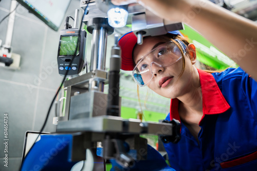 A female diesel engine mechanic in a blue uniform is working at the garage. Inspect and maintain the fuel pressure booster pump system and common rail injectors.