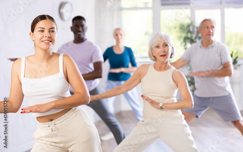 Young girl coach conducts classes for elderly in fitness studio. Female instructor teaches mature students of dance class basic movements of hip hop dance