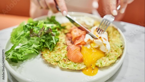 Stop Motion. Girl cuts poached egg and yolk flows out. Squash fritters, avocado cream with salmon and egg . Healthy breakfast, protein. Restaurant dish. 