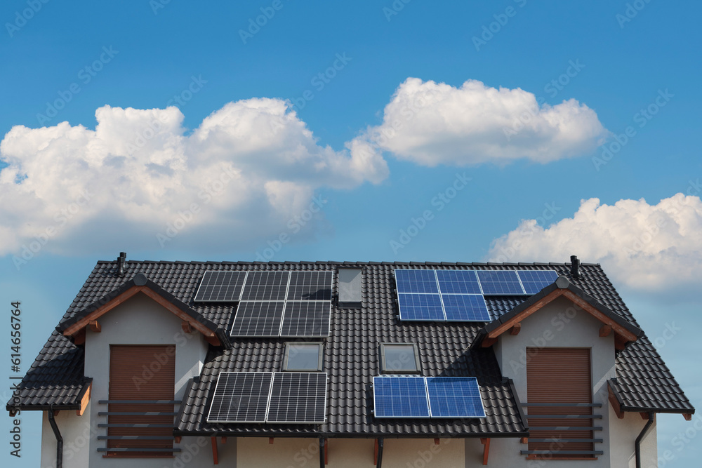 Black and blue solar panels mounted on the roof of a modern house.