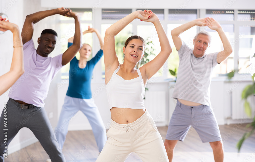 In fitness studio, youthful female coach is leading class for seniors. Instructor is teaching older students fundamental steps of hip hop dance in dance lesson