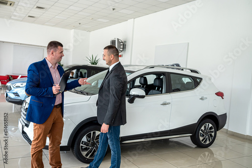 salesman with clipboard talking with his client about selling new modern car at dealershop © RomanR