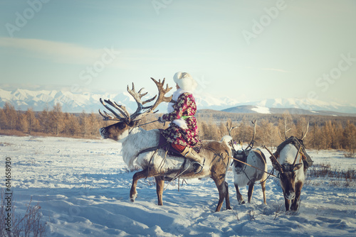 A Mongolian ethnic woman in traditional dress riding a deer with beautiful horns.