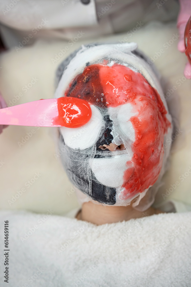female medical worker applying on face red alginate mask her client  in beauty salon