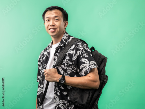 An Indonesian man (Asian) wearing a beach shirt and carrying a suitcase while smiling and posing. Isolated with a green background.