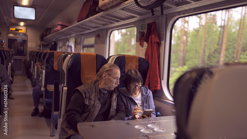 Elderly couple travel by train, the lady is holding a mobile phone in her hand, both are looking at the smartphone and talking with each other