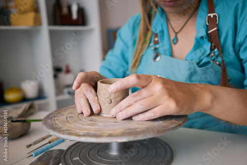 Craftswoman sculpting clay cup on pottery wheel at workshop photo