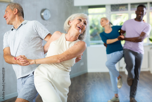 Active mature men and women practicing Rock 'n' Roll dance in training hall during dancing classes