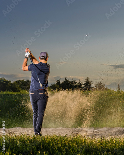 Man hitting golf ball on grass at dusk