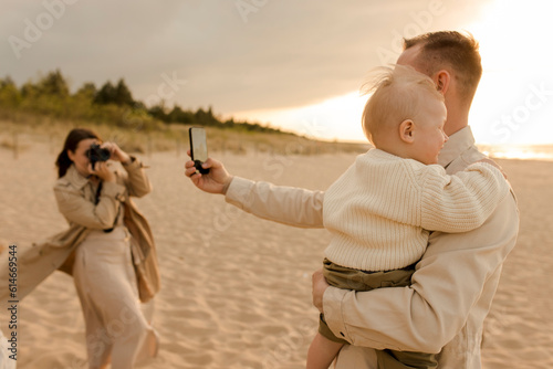 Father taking selfie with son and woman photographing through camera at beach photo