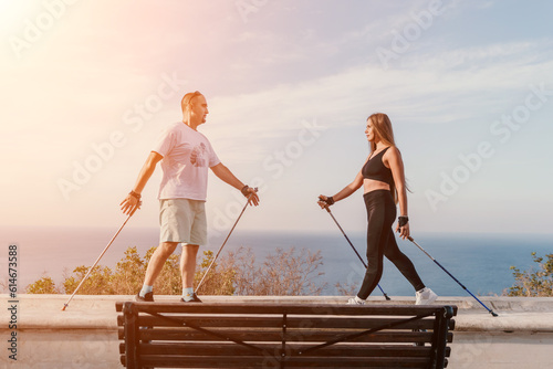 Happy Middle aged couple or friends practicing nordic walking in park near sea. Mature couple with trekking poles walking, practicing Nordic walking outdoors. Aging youthfully and sport concept photo
