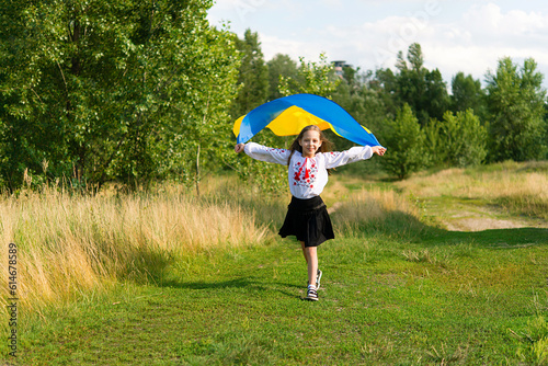 Ukrainian child girl with yellow and blue flag of Ukraine in field. Girl wearing national dress. Ukraines Independence Day. Constitution day.  Stand with Ukraine. photo