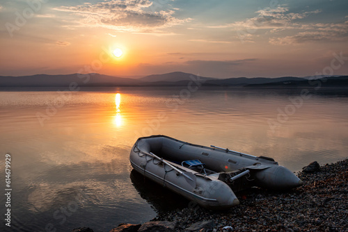 Rubber boat on the shore of the picturesque coast against the backdrop of sunset photo