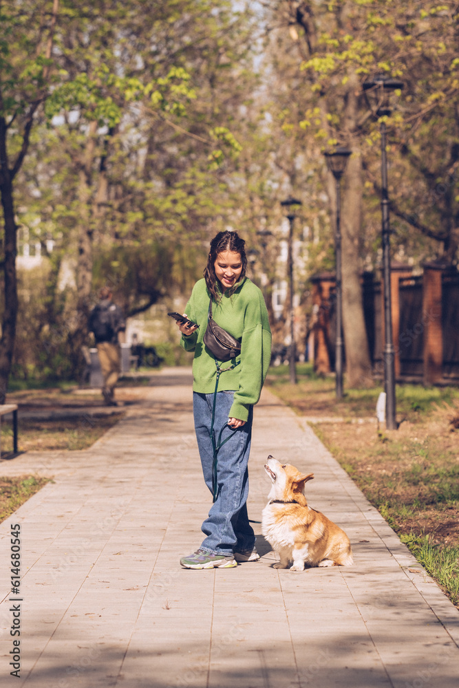 Fototapeta premium Portrait of a caucasian woman in green sweater and with corgi dog in a park