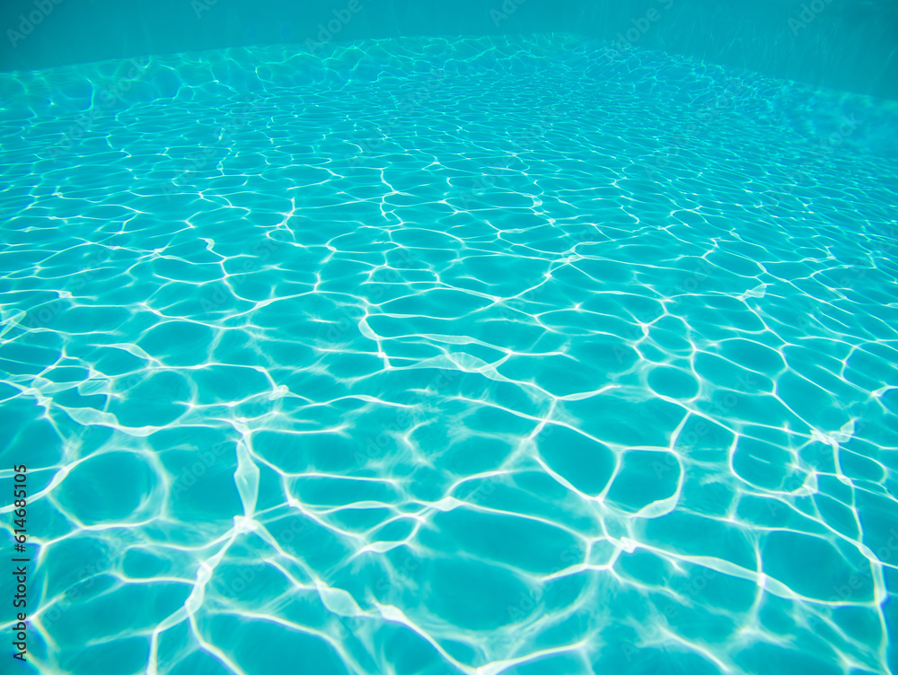 Blue swimming pool underwater with bright sun light reflections or caustics, background or texture.