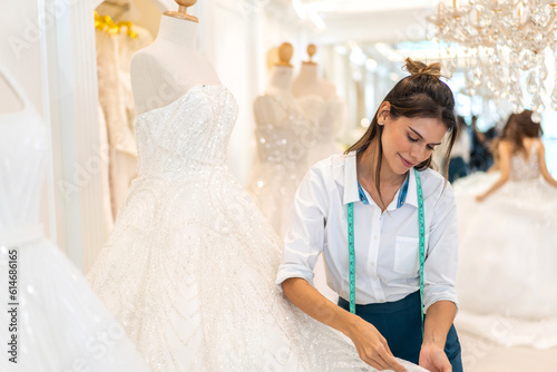 Portrait of entrepreneur bridal shop owner business woman fashion designer stylish working.Attractive designer girl using tape meter fitting on wedding dress with mannequin at wedding studio photo