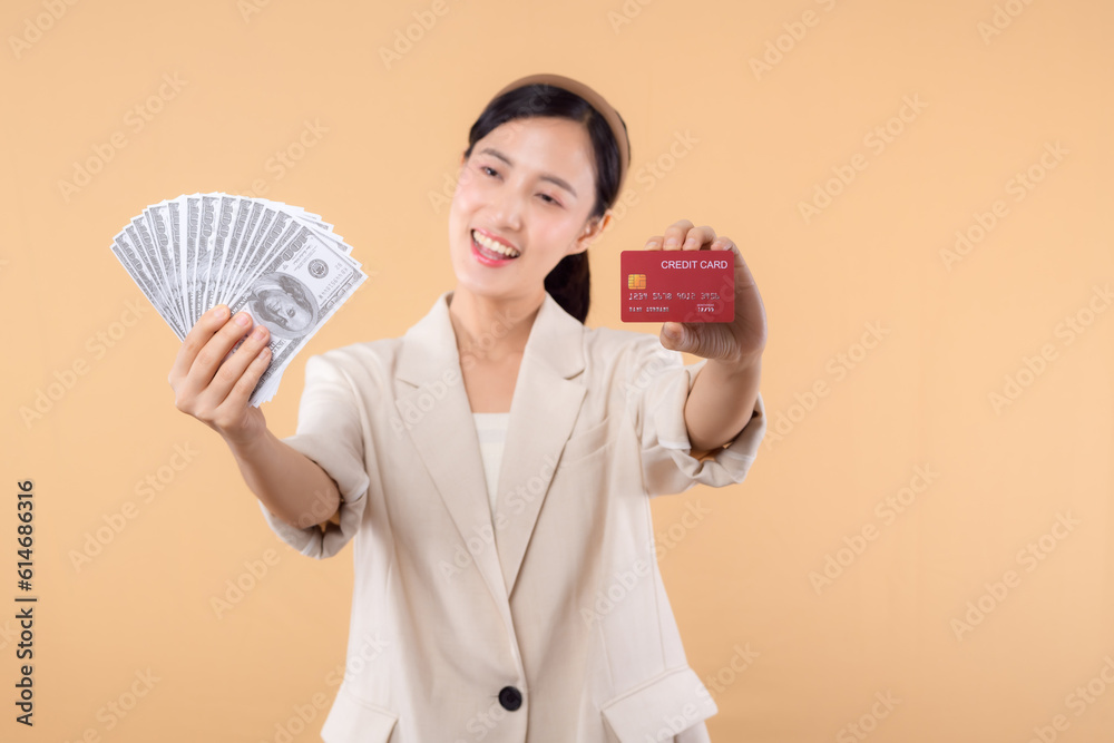 portrait of happy successful confident young asian business woman wearing white jacket holding cash money dollars and credit card standing over beige background. millionaire business, shopping concept portrait of happy successful confident young asian business woman wearing white jacket holding cash money dollars and credit card standing over beige background. millionaire business, shopping concept